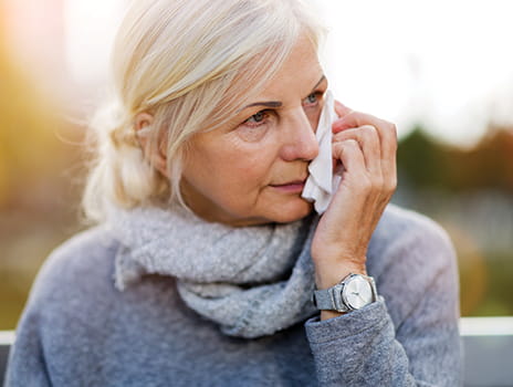 Older woman sitting outside dabbing her eyes with a tissue