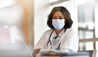 Female doctor wearing a mask while at computer
